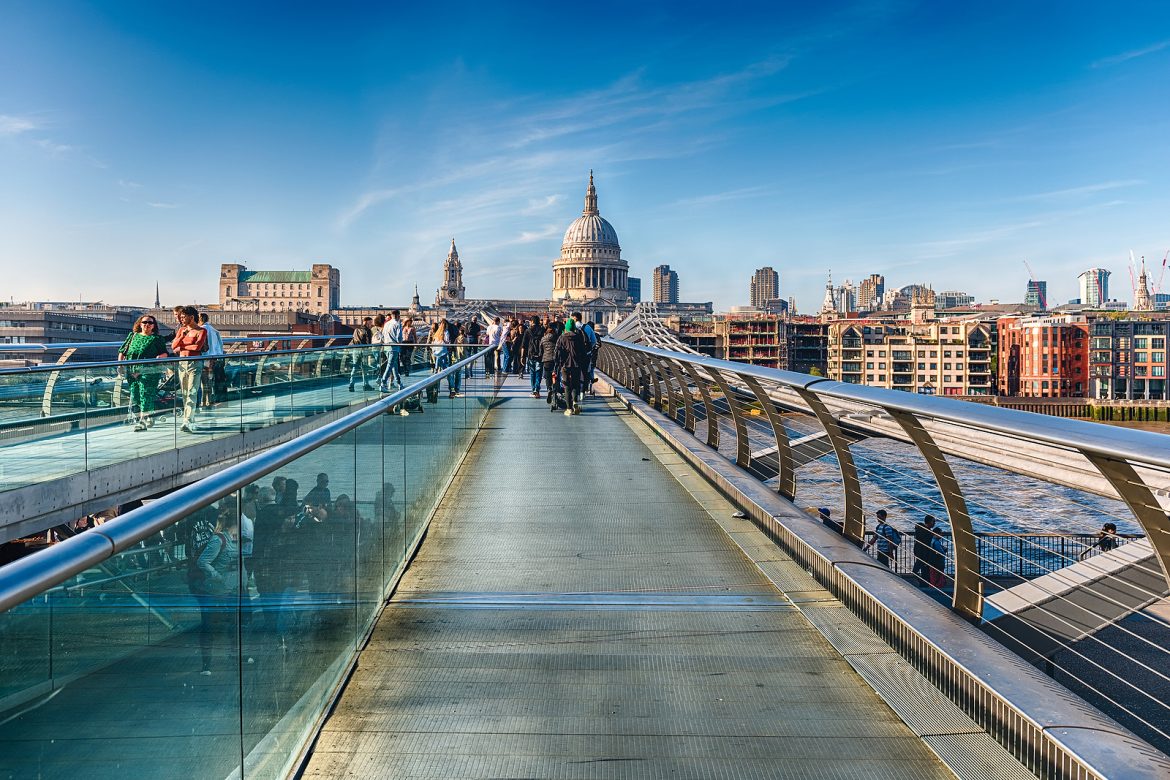 LONDON - APRIL 16, 2022: Walking on the Millennium Bridge, a steel suspension bridge for pedestrians crossing the River Thames in London, England, UK